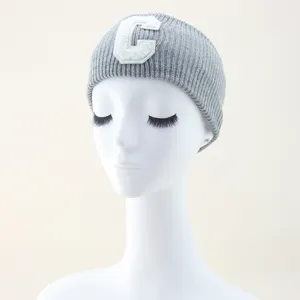 Dettaglio della fascia in maglia grigia con patch lettera C bianca, accessorio per capelli.