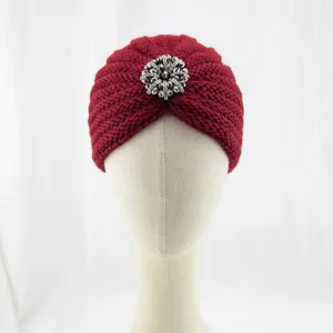 Close-up detail of the elegant red knit turban featuring a sparkling silver rhinestone brooch accent.
