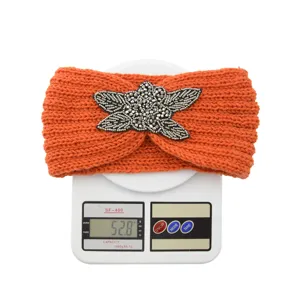 Orange knitted headband with rhinestone four-leaf detail, warm winter hair accessory.