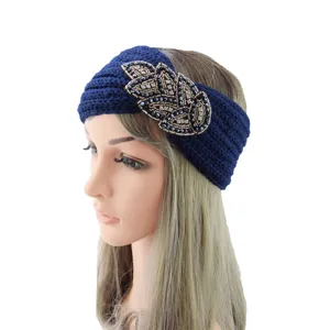 Detail shot of dark blue knitted wool headband with sparkly rhinestone leaf accessory for warmth.