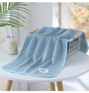 Detailansicht des dicken Korallenfleece-Handtuchs mit eleganter G-Stickerei im Bad.