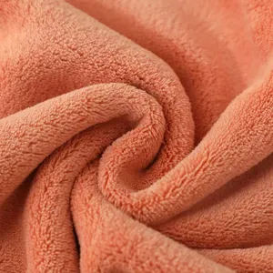 Zachte koraalvleece handdoekstof close-up, pluche textuur, gezellig absorberend badhanddoekmateriaal.