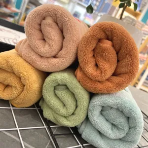 Soft coral fleece face towels rolled neatly, colorful fluffy absorbent daily bath towels.
