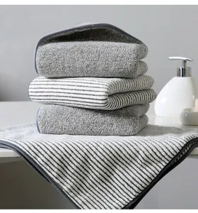Detailed view of thick coral velvet striped and grey towels stacked on clean white surface.