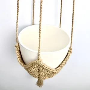 Gedetailleerde close-up van handgemaakte boho jute plantenhanger met witte pot en kwast.
