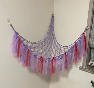 Handmade woven corner toy hammock for kids room, purple macrame net with colorful ribbons.