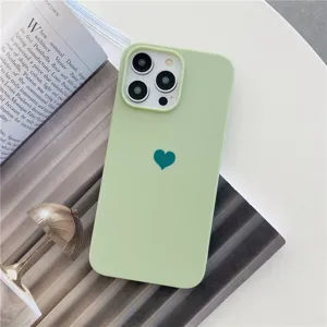 Gros plan de la coque de téléphone mate vert clair avec motif cœur vert foncé sur table.