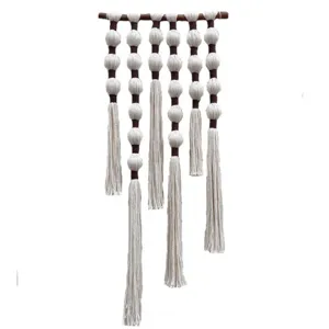 Handgemaakte macrame wandhanger met houten stok en witte ballen voor interieurdecoratie.