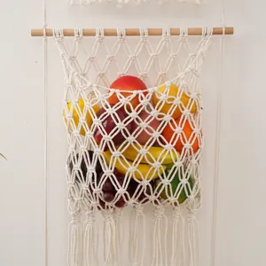 Macrame fruit hammock detail, bohemian cotton rope hanging basket for kitchen wall storage.