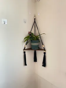 Détail d'étagère d'angle murale avec planchette en bois et corde en coton noir bien suspendue.