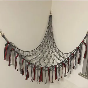 Handmade macrame toy hammock for corner wall storage, grey cotton net with festive ribbons.