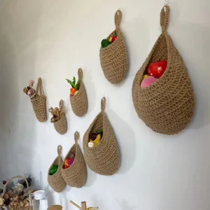 Handmade jute hanging basket for kitchen wall storage, rustic woven fruit vegetable pocket organizer.
