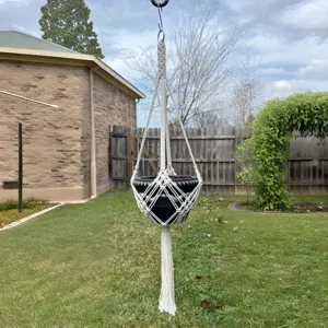 Vue détaillée d'un porte-plante en macramé de coton blanc fait main dans un jardin.