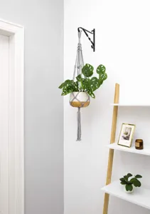 Handgemaakte grijze macramé plantenhanger met keramische pot voor wanddecoratie thuis.