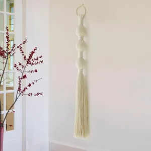 Handgemaakte macramé wandhang van katoen met bolletjes en kwastje voor stijlvolle huisdecoratie.