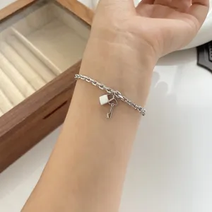 Detailopname van een zilverkleurige kettingarmband met slot- en sleutelhangers om de pols.