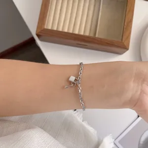 Detail van zilveren armband met hangslot en sleutel, minimalistisch en elegant sieraad.