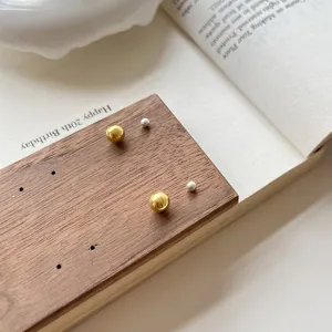 Detail shot of minimalist gold and silver ball stud earrings displayed on wooden card.