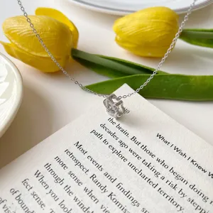 Detailed shot of silver clavicle necklace with sparkling pendant on book and floral decor.