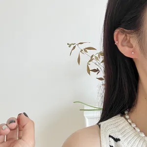 Close-up detail shot of minimal sterling silver small round ball stud earrings worn on ear.