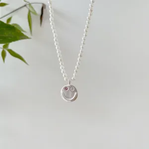 Zarte Perlenkette mit mattem Silber-Smile-Anhänger und funkelnden Zirkoniasteinen als Augen.