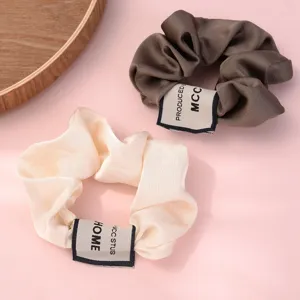 Satin hair scrunchies set in dark brown and beige with stylish fabric labels for elegant hairstyles.