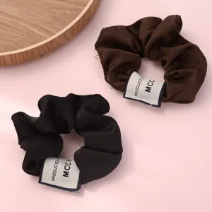 Detail shot of elegant brown and black satin hair scrunchies with chic label design for women.