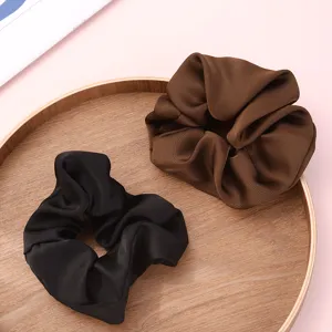 Close-up detail of stylish satin hair scrunchies in black and brown colors on a tray.
