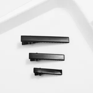 Detailed view of three black metal alligator hair clips arranged by size on white tray.