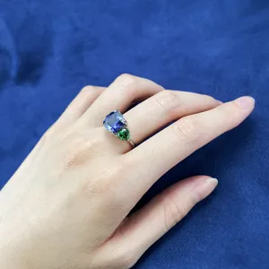 Primo piano dettagliato di anello in tanzanite blu con gemma verde indossato a mano.