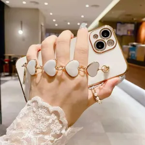 Vista detallada de funda de teléfono con cadena de corazón blanco, elegante accesorio de pulsera dorada.