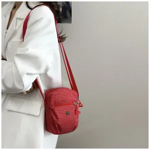 Detail view of red plaid crossbody bag featuring front zipper pocket and adjustable strap.