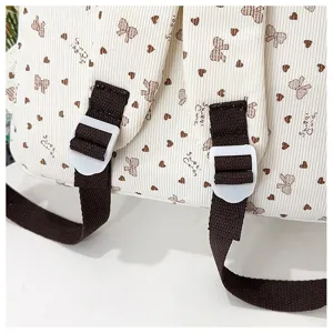 Corduroy backpack detail showing bow heart print, brown straps and white buckle.