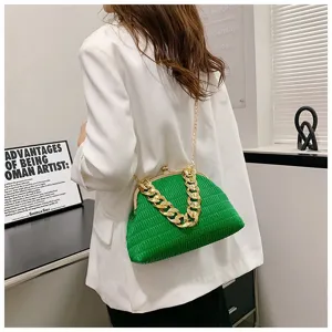 Green pleated clutch bag detail showing chunky gold chain and frame closure in stylish scene.
