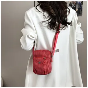 Detailed view of a stylish red plaid crossbody bag with zipper pocket and adjustable strap.