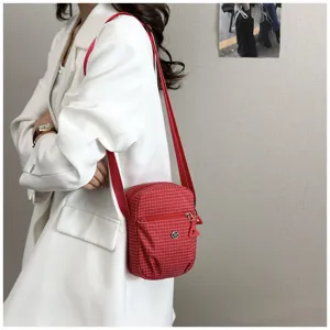 Detailed view of red plaid crossbody bag worn with white blazer, compact fabric shoulder purse.