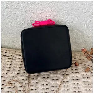 Detail view of the stylish black mini crossbody bag with gold chain and neon pink bow.