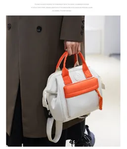 Detailed view of the stylish white mommy backpack with vibrant orange pockets and braided charm.