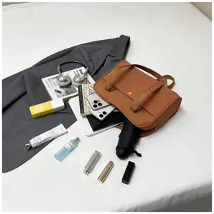 Detailed capacity showcase of brown canvas shoulder bag with various daily items layout on white sheet.
