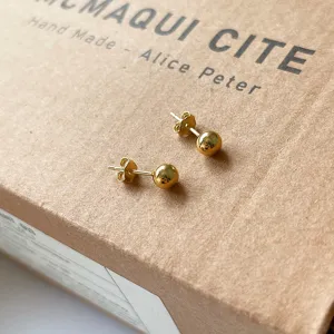 Nahaufnahme minimalistischer goldener Kugel-Ohrstecker auf Packpapier, schlichter eleganter Schmuck.