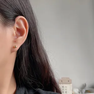 Nahaufnahme Detail eines minimalistischen kleinen runden Kugel-Ohrrings am Ohr, eleganter Stil.