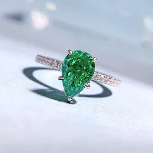 Dettaglio in primo piano di anello in argento con gemma verde a pera e fascia pavimentata.