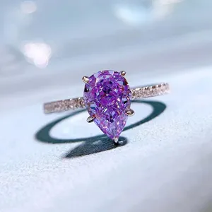 Squisito primo piano di un anello con gemma viola taglio a pera e fascia di diamanti.