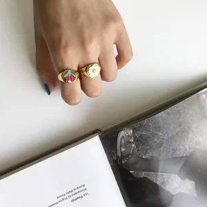 Nahaufnahme stilvoller Goldringe mit buntem Emaille-Tulpen- und Gänseblümchen-Design.