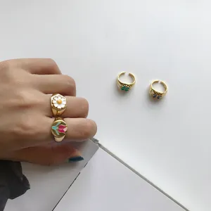 Detailansicht bunter Emaillierungsringe mit Blumen- und Kleeblattmotiven auf der Hand.