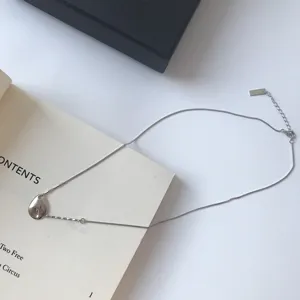 Detaillierte Nahaufnahme der silbernen Box-Kette mit einem unregelmassigen Anhaenger auf Buch.