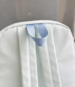 Detail view of the top handle and reinforced shoulder straps on a light green casual backpack.