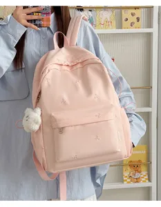 Pink school backpack detail showing cute bow embroidery and plush bear pendant accessory.