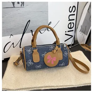 Detailed view of casual denim barrel pillow bag with chic bow prints and brown leather trim.