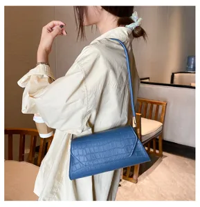Detailaufnahme einer blauen Kroko-Muster-Schultertasche im Baguette-Stil am Model.